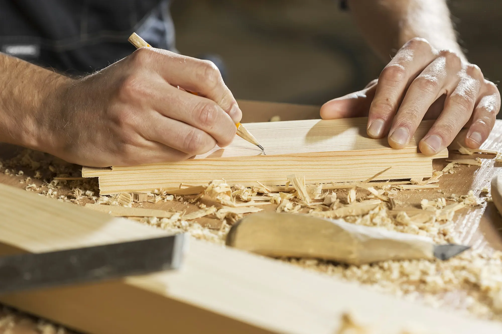 A carpenter marks a line in pencil on a board