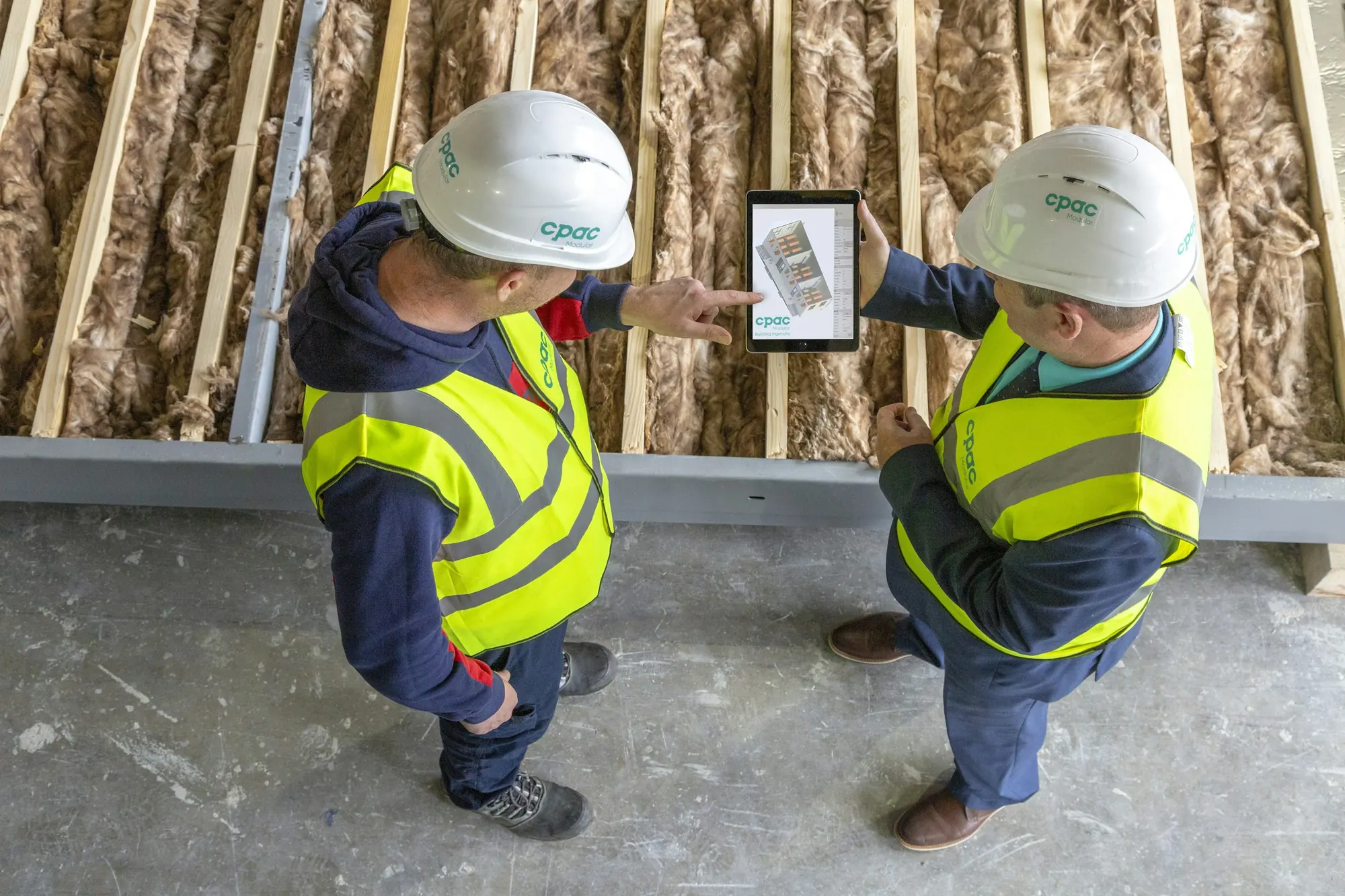 Two workers review plans on a tablet on site